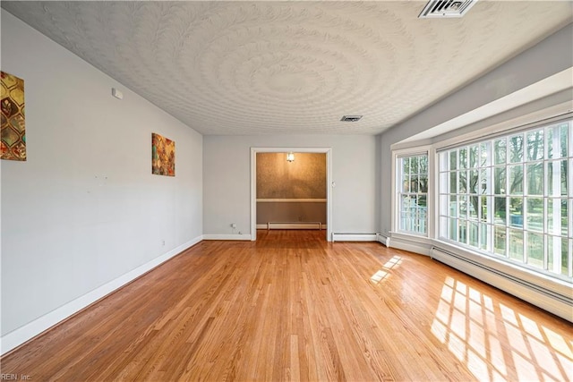 unfurnished room with baseboards, visible vents, light wood finished floors, and a baseboard radiator