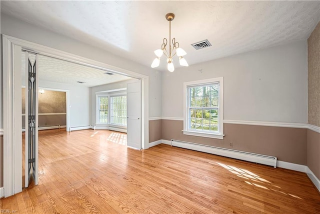 unfurnished room with light wood finished floors, a notable chandelier, plenty of natural light, and baseboard heating