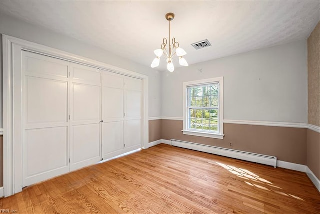 unfurnished bedroom featuring a baseboard heating unit, baseboards, a chandelier, light wood-style flooring, and a closet