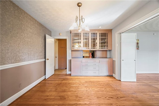 unfurnished dining area with a chandelier, light wood-type flooring, and baseboards