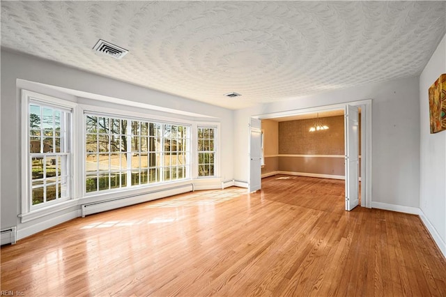 interior space with visible vents, a textured ceiling, light wood finished floors, baseboard heating, and a chandelier