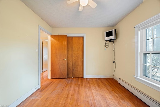 unfurnished bedroom with a baseboard heating unit, baseboards, ceiling fan, and light wood finished floors