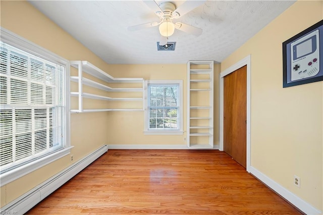 spare room featuring visible vents, light wood-style flooring, baseboards, baseboard heating, and ceiling fan