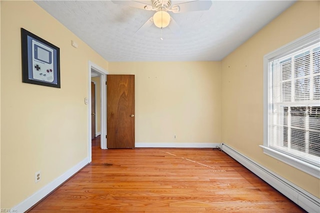 empty room featuring baseboards, plenty of natural light, baseboard heating, and light wood finished floors