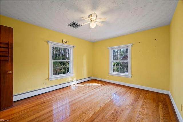 empty room with visible vents, baseboards, wood finished floors, a ceiling fan, and a baseboard radiator