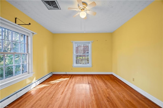 spare room featuring light wood-type flooring, plenty of natural light, visible vents, and a baseboard radiator