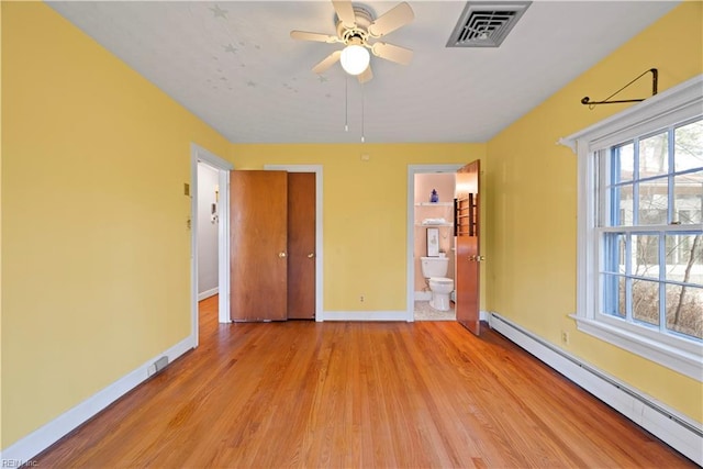 unfurnished bedroom featuring baseboards, visible vents, light wood finished floors, a baseboard heating unit, and connected bathroom