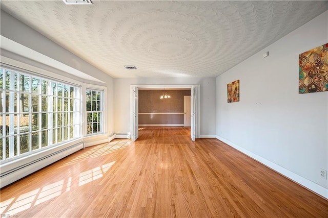 unfurnished room with visible vents, baseboards, baseboard heating, light wood-style flooring, and an inviting chandelier