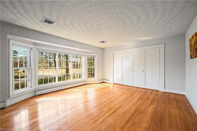 unfurnished bedroom with visible vents, a textured ceiling, light wood finished floors, baseboards, and baseboard heating