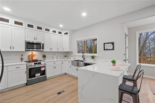 kitchen with a kitchen bar, a peninsula, stainless steel appliances, white cabinetry, and a sink