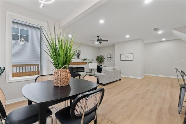 dining area with baseboards, recessed lighting, light wood-style floors, a glass covered fireplace, and a ceiling fan