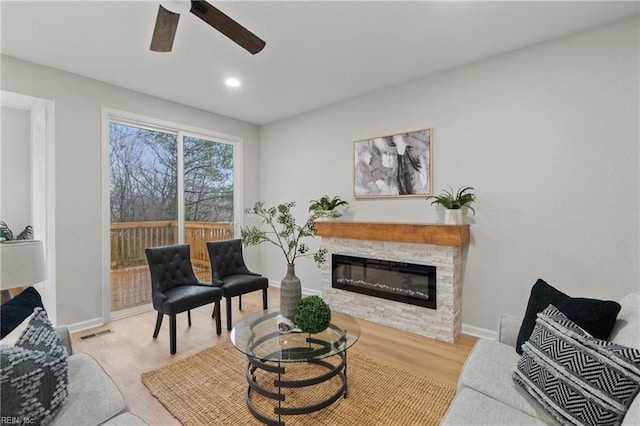 living area with visible vents, a glass covered fireplace, wood finished floors, baseboards, and ceiling fan