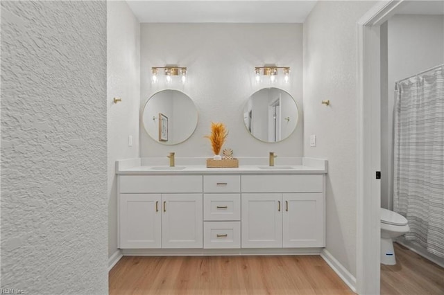 bathroom featuring double vanity, toilet, wood finished floors, and a sink