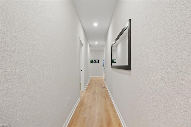 hallway with baseboards, light wood-style floors, and a textured wall