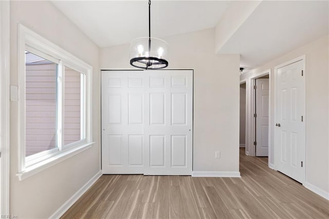 unfurnished bedroom featuring light wood-style flooring, baseboards, and an inviting chandelier