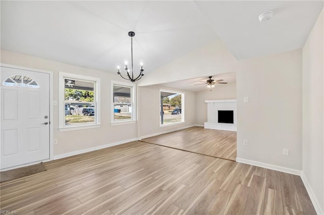 unfurnished living room with vaulted ceiling, a fireplace with raised hearth, light wood-type flooring, and a healthy amount of sunlight