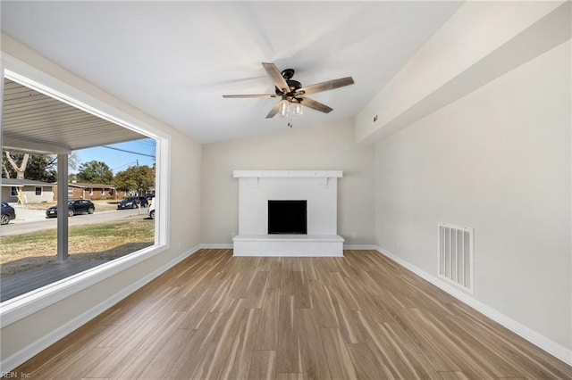 unfurnished living room featuring visible vents, a brick fireplace, baseboards, lofted ceiling, and wood finished floors