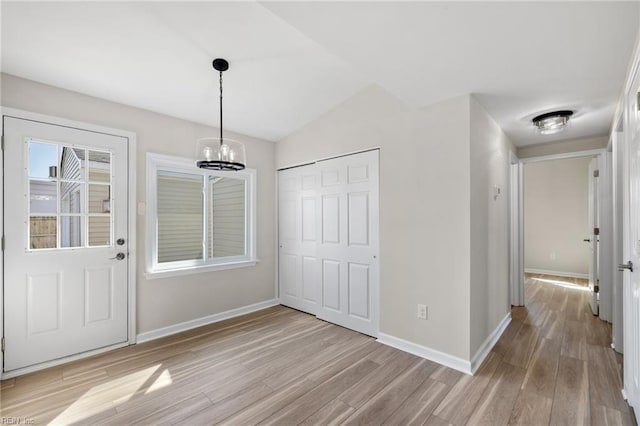 unfurnished dining area featuring baseboards, lofted ceiling, a chandelier, and light wood finished floors