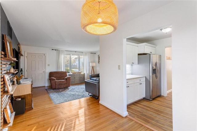 interior space with light wood-style flooring, open floor plan, stainless steel fridge with ice dispenser, and white cabinets