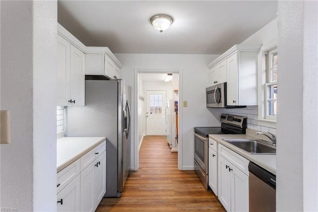 kitchen with light countertops, appliances with stainless steel finishes, wood finished floors, white cabinetry, and a sink