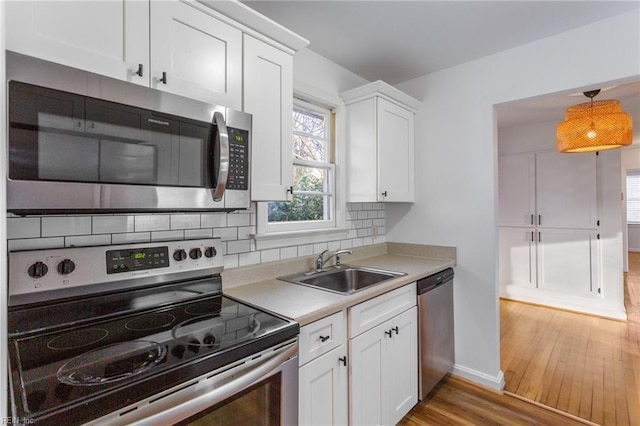 kitchen featuring light wood-type flooring, a sink, tasteful backsplash, stainless steel appliances, and white cabinets