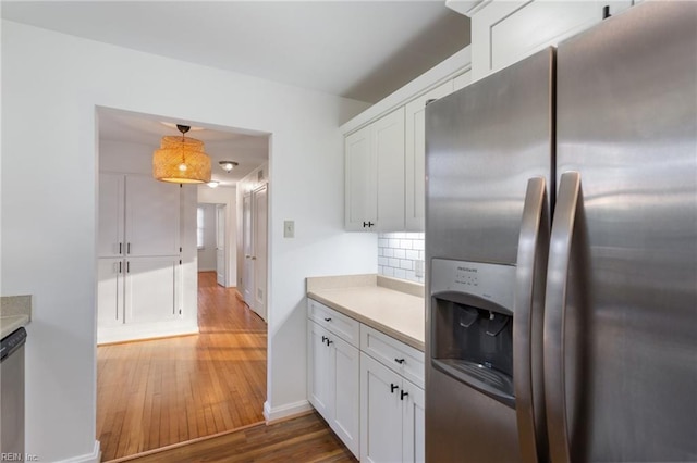 kitchen with stainless steel fridge with ice dispenser, light countertops, decorative backsplash, wood finished floors, and white cabinetry