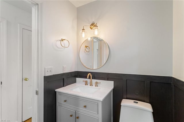 bathroom featuring a wainscoted wall, toilet, vanity, and a decorative wall