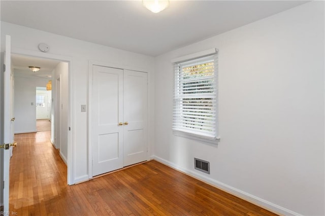 unfurnished bedroom with baseboards, visible vents, wood-type flooring, and a closet