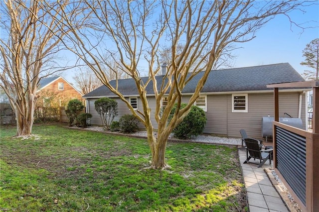 rear view of property with a lawn, roof with shingles, and fence