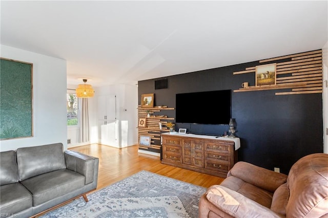 living area with visible vents, an accent wall, and wood finished floors