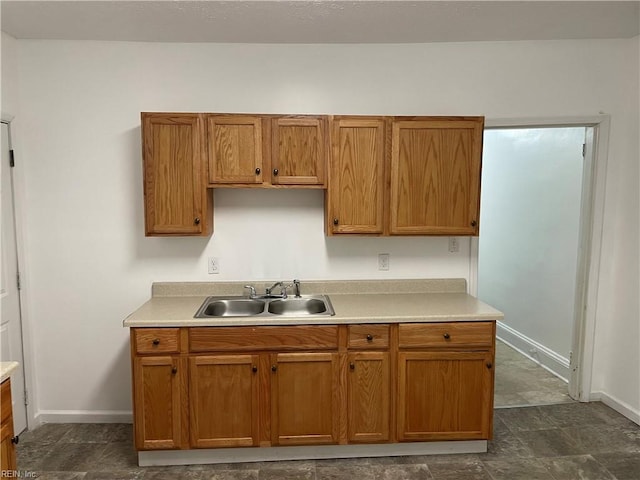 kitchen with light countertops, baseboards, brown cabinets, and a sink