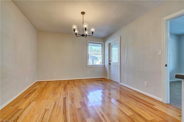 empty room with baseboards, a notable chandelier, light wood-style flooring, and a textured ceiling