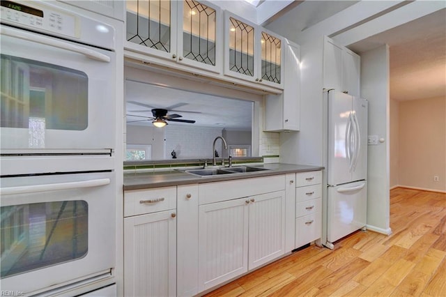 kitchen with light wood-type flooring, a sink, white appliances, white cabinets, and glass insert cabinets