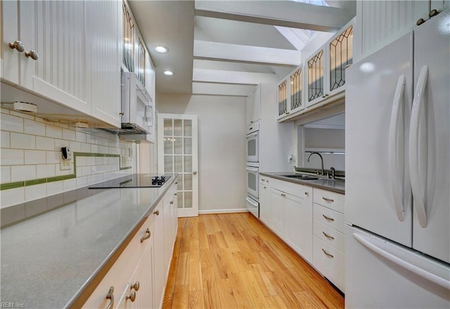 kitchen featuring white appliances, a sink, glass insert cabinets, light wood-type flooring, and backsplash