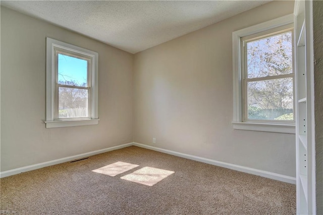 carpeted empty room featuring visible vents, a textured ceiling, and baseboards