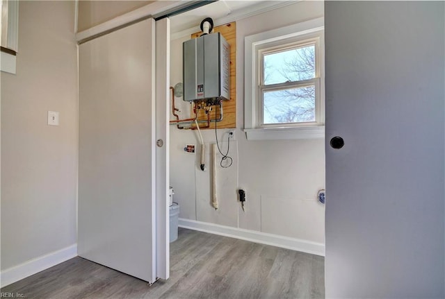 laundry area with wood finished floors, tankless water heater, and baseboards