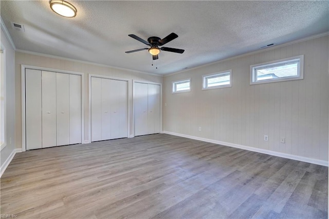 unfurnished bedroom with visible vents, two closets, wood finished floors, and ornamental molding