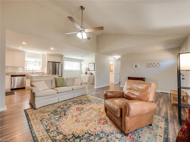 living room featuring baseboards, light wood-style floors, ceiling fan, and vaulted ceiling