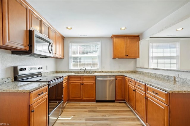 kitchen with light stone counters, light wood finished floors, a peninsula, a sink, and appliances with stainless steel finishes