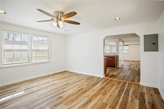 empty room featuring a ceiling fan, baseboards, electric panel, recessed lighting, and light wood-style floors