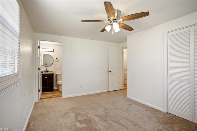 unfurnished bedroom featuring ensuite bath, a closet, carpet, baseboards, and ceiling fan