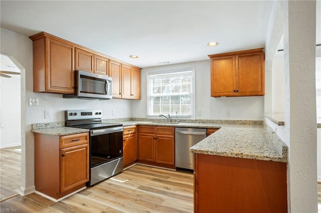 kitchen featuring a sink, arched walkways, light wood finished floors, and stainless steel appliances