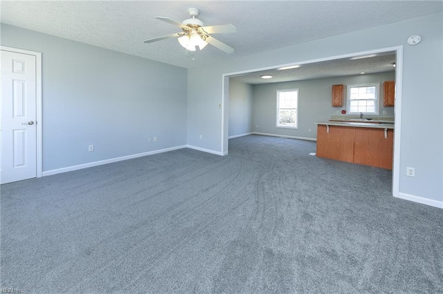 unfurnished living room featuring dark colored carpet, baseboards, a textured ceiling, and ceiling fan