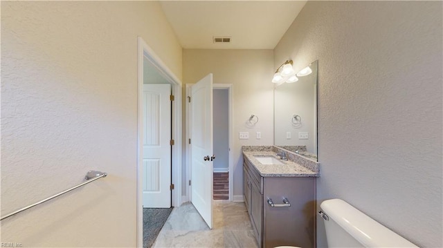 bathroom featuring vanity, toilet, a textured wall, and visible vents