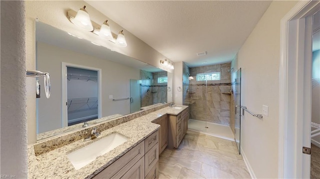 full bath with a walk in closet, a stall shower, a textured ceiling, baseboards, and vanity