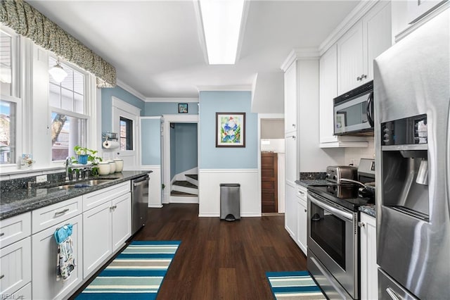 kitchen featuring wainscoting, stainless steel appliances, dark wood-style floors, white cabinetry, and a sink