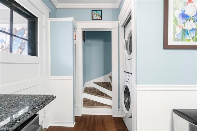 clothes washing area with dark wood finished floors, stacked washer and clothes dryer, ornamental molding, and laundry area