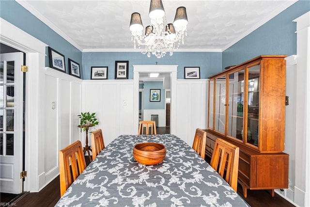 dining area featuring a chandelier, a wainscoted wall, dark wood-type flooring, and ornamental molding