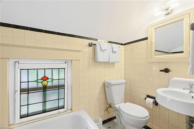 bathroom featuring a sink, a tub to relax in, toilet, and tile walls