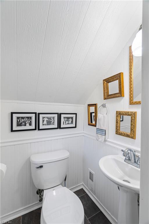 half bath featuring tile patterned flooring, visible vents, toilet, vaulted ceiling, and a sink